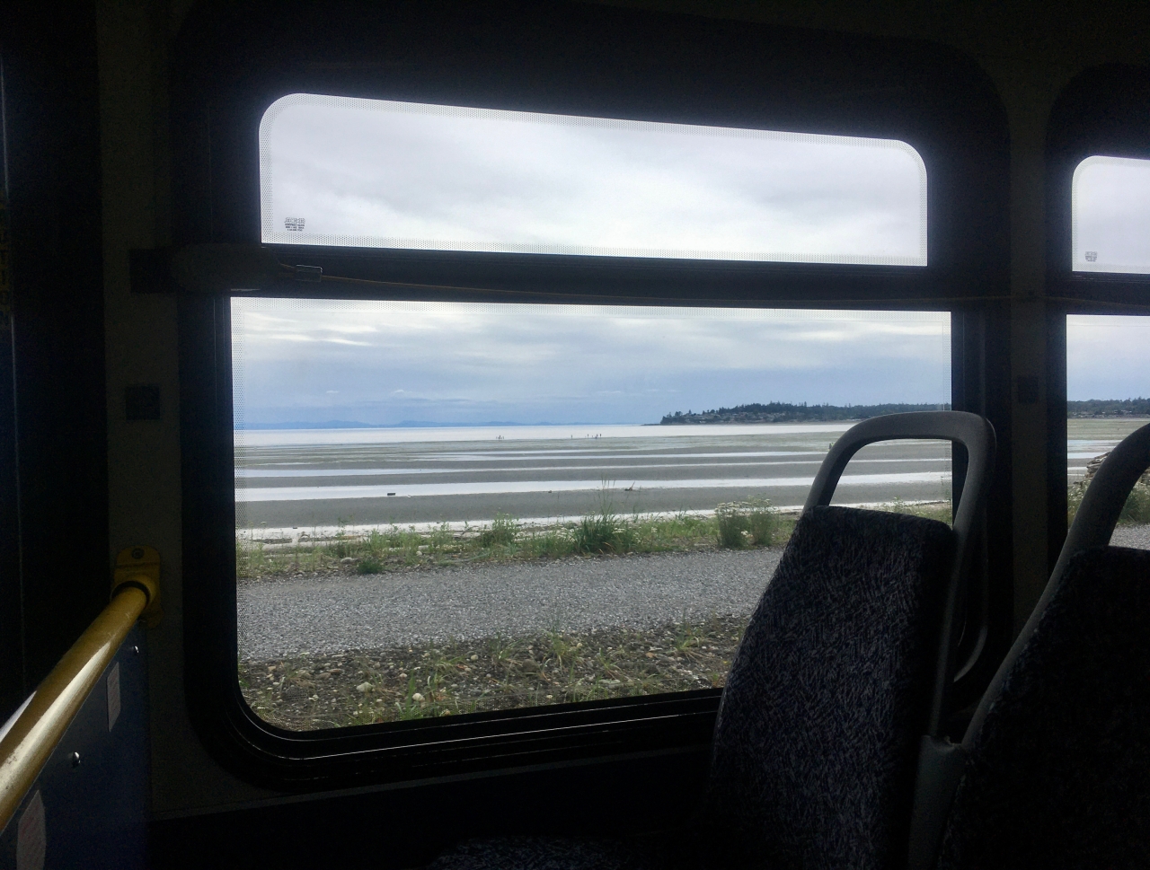 The view out to Birch Bay from a Whatcom Transportation Authority bus. The tide is low so the shoreline is off in the distance. It's a cloudy day and a peninsula sits off in the distance on the right.
